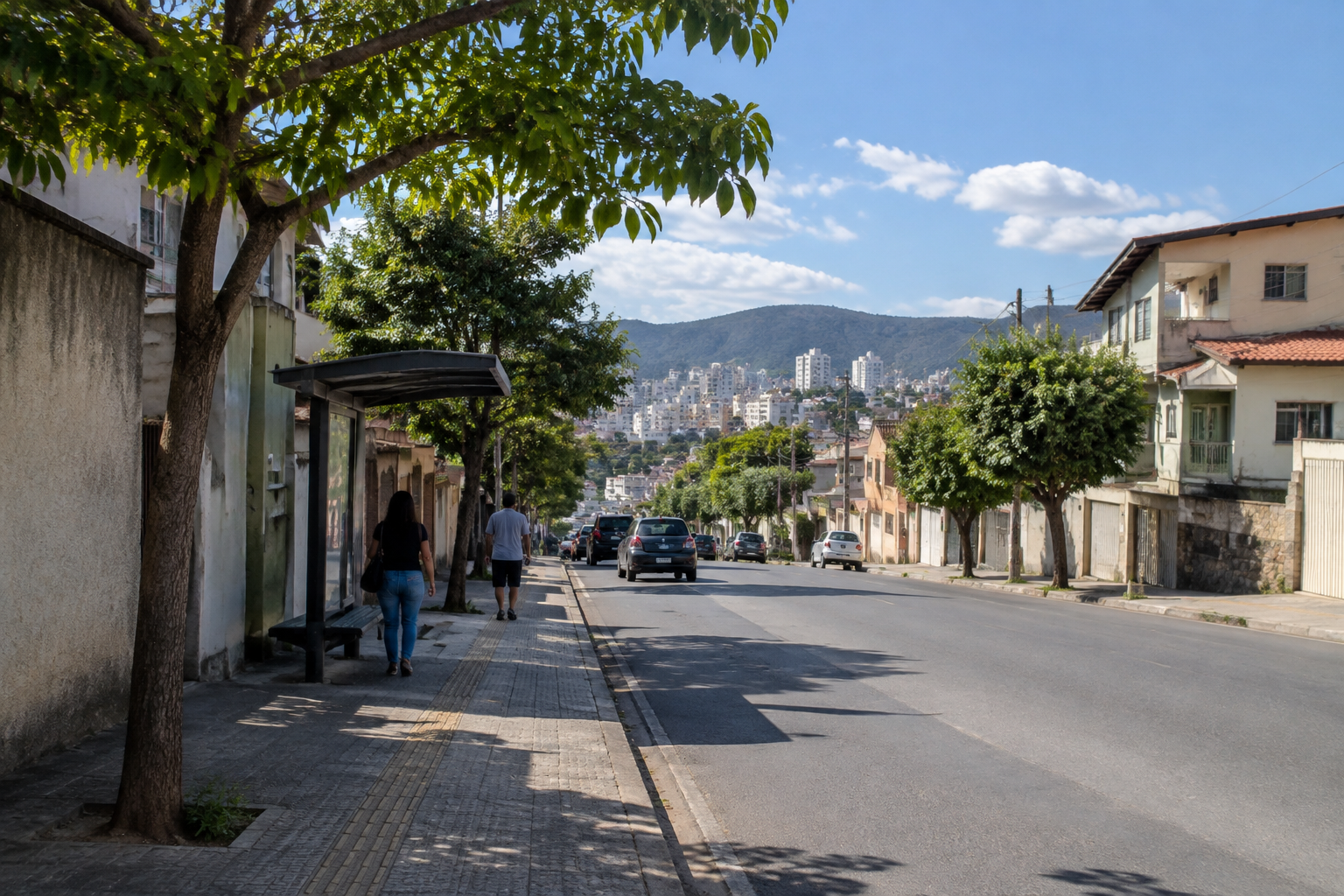 Rua urbana em Minas Gerais sob sol e poucas nuvens, com calçada sombreada e ponto de ônibus.
